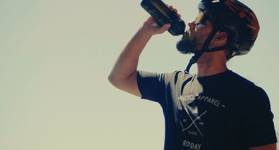 Mannelijke wielrenner hydrateert met Isostar bidon tijdens een mountainbikewedstrijd